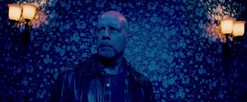 Movie still from “Surrogates” (2009), directed by Jonathan Mostow – A man with a beard is standing in front of a wall with flowers; Medium shot, Low angle