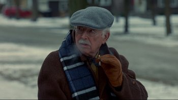 Movie still from “Surviving Christmas” (2004), directed by Mike Mitchell – An old man smoking a cigarette while wearing a scarf; Close Up shot, Over the shoulder angle