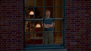 Movie still from “Surviving Christmas” (2004), directed by Mike Mitchell – A man standing in front of an open window with his arms crossed; Wide shot, Low angle