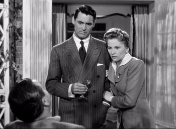 Movie still from “Suspicion” (1941), directed by Alfred Hitchcock – A man and a woman standing next to each other holding wine glasses; Medium shot, Over the shoulder angle