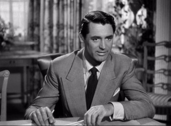 Movie still from “Suspicion” (1941), directed by Alfred Hitchcock – A man sitting at a table wearing a suit and tie; Medium shot, Over the shoulder angle