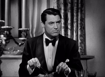 Movie still from “Suspicion” (1941), directed by Alfred Hitchcock – A man wearing a tuxedo and a bow tie holding a knife; Close Up shot, Over the shoulder angle