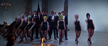 Movie still from “Sweet Charity” (1969), directed by Bob Fosse – A group of people standing next to each other in front of a fire pit; Wide shot, Low angle