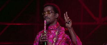Movie still from “Sweet Charity” (1969), directed by Bob Fosse – A man in a pink shirt holding a pipe and making a peace sign; Close Up shot, Low angle