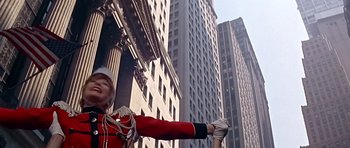 Movie still from “Sweet Charity” (1969), directed by Bob Fosse – A man in a red jacket and a white hat is standing in front of a tall building; Medium shot, Low angle