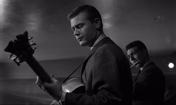 Movie still from “Sweet Smell of Success” (1957), directed by Alexander Mackendrick – A black and white photo of a man holding a guitar; Close Up shot, Low angle