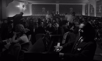 Movie still from “Sweet Smell of Success” (1957), directed by Alexander Mackendrick – A group of people sitting around a piano in a room; Medium shot, High angle