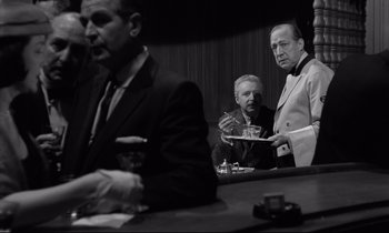 Movie still from “Sweet Smell of Success” (1957), directed by Alexander Mackendrick – A group of men sitting at a table in front of a bar; Medium shot, Over the shoulder angle