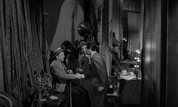 Movie still from “Sweet Smell of Success” (1957), directed by Alexander Mackendrick – A man shaking hands with another man in front of a camera; Medium shot, High angle