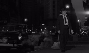 Movie still from “Sweet Smell of Success” (1957), directed by Alexander Mackendrick – A man in a suit and hat holding a vacuum next to an old car; Wide shot, Low angle