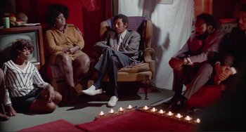 Movie still from “Sweet Sweetback's Baadasssss Song” (1971), directed by Melvin Van Peebles – A group of people sitting in a room with candles; Wide shot, High angle