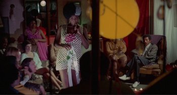 Movie still from “Sweet Sweetback's Baadasssss Song” (1971), directed by Melvin Van Peebles – A woman that is standing up in front of a group of people; Wide shot, Over the shoulder angle