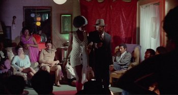 Movie still from “Sweet Sweetback's Baadasssss Song” (1971), directed by Melvin Van Peebles – A man and a woman are on stage in a living room; Wide shot, Over the shoulder angle