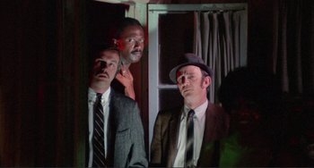 Movie still from “Sweet Sweetback's Baadasssss Song” (1971), directed by Melvin Van Peebles – A group of men standing next to each other in front of a window; Medium shot, Low angle