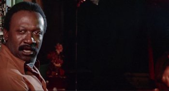 Movie still from “Sweet Sweetback's Baadasssss Song” (1971), directed by Melvin Van Peebles – A man standing in front of a microphone in a dark room; Close Up shot, Low angle