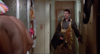 Movie still from “Sweet Sweetback's Baadasssss Song” (1971), directed by Melvin Van Peebles – A man in a suit is standing in front of a bathroom mirror; Medium shot, Over the shoulder angle