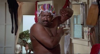 Movie still from “Sweet Sweetback's Baadasssss Song” (1971), directed by Melvin Van Peebles – A man in a shower cap is holding his arm up; Medium shot, Low angle