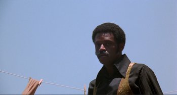Movie still from “Sweet Sweetback's Baadasssss Song” (1971), directed by Melvin Van Peebles – A man with a beard and a black shirt is standing on a clothesline; Medium shot, Low angle
