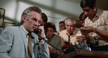 Movie still from “Sweet Sweetback's Baadasssss Song” (1971), directed by Melvin Van Peebles – A group of men standing around each other on the phone; Medium shot, Low angle