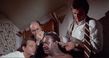 Movie still from “Sweet Sweetback's Baadasssss Song” (1971), directed by Melvin Van Peebles – A man getting his hair cut by two other men; Medium shot, High angle
