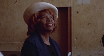 Movie still from “Sweet Sweetback's Baadasssss Song” (1971), directed by Melvin Van Peebles – An older woman wearing a white hat in a room; Close Up shot, Low angle