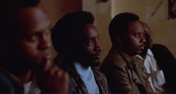 Movie still from “Sweet Sweetback's Baadasssss Song” (1971), directed by Melvin Van Peebles – A group of men sitting next to each other in a room; Close Up shot, Over the shoulder angle