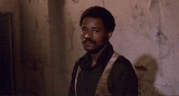 Movie still from “Sweet Sweetback's Baadasssss Song” (1971), directed by Melvin Van Peebles – A man with a beard and mustache wearing a black shirt; Close Up shot, Low angle