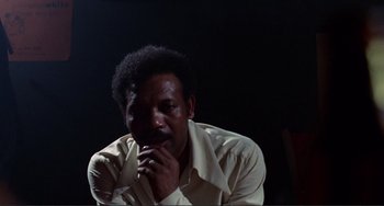 Movie still from “Sweet Sweetback's Baadasssss Song” (1971), directed by Melvin Van Peebles – A man with a beard is sitting in a dark room; Close Up shot, Low angle
