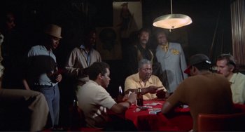 Movie still from “Sweet Sweetback's Baadasssss Song” (1971), directed by Melvin Van Peebles – A group of men sitting at a table playing cards; Wide shot, Over the shoulder angle