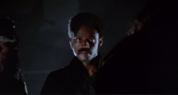Movie still from “Sweet Sweetback's Baadasssss Song” (1971), directed by Melvin Van Peebles – A man in a dark room with a beard and mustache; Close Up shot, Over the shoulder angle