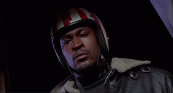 Movie still from “Sweet Sweetback's Baadasssss Song” (1971), directed by Melvin Van Peebles – A person wearing a motorcycle helmet; Close Up shot, Low angle