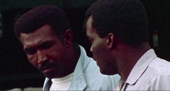 Movie still from “Sweet Sweetback's Baadasssss Song” (1971), directed by Melvin Van Peebles – Two men are talking to each other outside; Close Up shot, Low angle