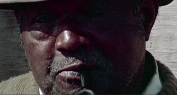 Movie still from “Sweet Sweetback's Baadasssss Song” (1971), directed by Melvin Van Peebles – A man's face while smoking a pipe; Extreme Close Up shot, Low angle