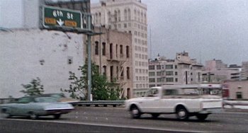 Movie still from “Sweet Sweetback's Baadasssss Song” (1971), directed by Melvin Van Peebles – A white truck driving down a street next to tall buildings; Extreme Wide shot, High angle