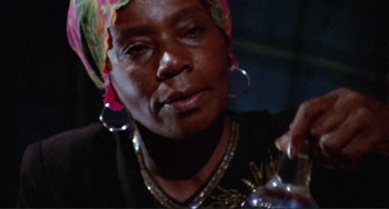 Movie still from “Sweet Sweetback's Baadasssss Song” (1971), directed by Melvin Van Peebles – An older woman wearing a colorful headscarf and earrings; Close Up shot, Low angle