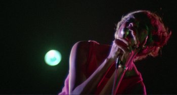 Movie still from “Sweet Sweetback's Baadasssss Song” (1971), directed by Melvin Van Peebles – A person holding a microphone up to their mouth; Medium shot, Low angle
