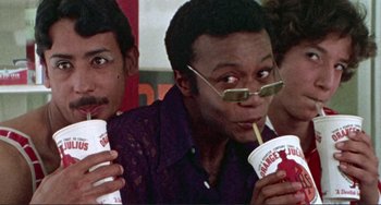 Movie still from “Sweet Sweetback's Baadasssss Song” (1971), directed by Melvin Van Peebles – A group of men sitting next to each other holding drinks; Close Up shot, High angle