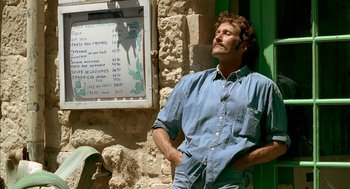 Movie still from “Swimming Pool” (2003), directed by François Ozon – A man standing in front of a building with his hands in his pockets; Medium shot, Low angle