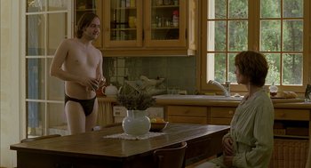 Movie still from “Swimming Pool” (2003), directed by François Ozon – A man standing in front of a woman in a kitchen; Medium shot, Over the shoulder angle