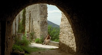 Movie still from “Swimming Pool” (2003), directed by François Ozon – Two people sitting on a bench in front of an archway; Extreme Wide shot, Over the shoulder angle