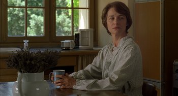 Movie still from “Swimming Pool” (2003), directed by François Ozon – A woman sitting at a table holding a mug; Medium shot, Over the shoulder angle
