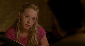 Movie still from “Swimming Pool” (2003), directed by François Ozon – A young woman is sitting at a table looking at the camera; Close Up shot, Over the shoulder angle