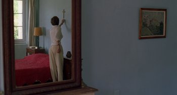 Movie still from “Swimming Pool” (2003), directed by François Ozon – A woman standing in front of a mirror holding a cross; Medium shot, Over the shoulder angle
