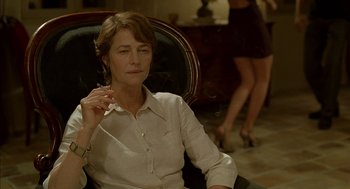 Movie still from “Swimming Pool” (2003), directed by François Ozon – A woman sitting in a chair with a cigarette in her mouth; Medium shot, Over the shoulder angle