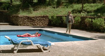 Movie still from “Swimming Pool” (2003), directed by François Ozon – A woman is standing by a pool and a man is lying on the ground; Wide shot, Over the shoulder angle