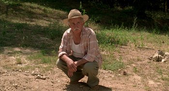 Movie still from “Swimming Pool” (2003), directed by François Ozon – An old man squatting on the ground in the dirt; Medium shot, High angle