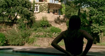 Movie still from “Swimming Pool” (2003), directed by François Ozon – A woman sitting in a swimming pool near a house; Extreme Wide shot, Over the shoulder angle