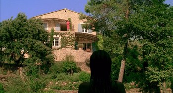 Movie still from “Swimming Pool” (2003), directed by François Ozon – A woman is standing in front of a stone house; Extreme Wide shot, Low angle