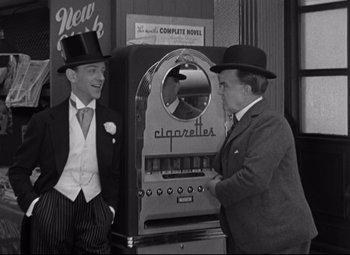 Movie still from “Swing Time” (1936), directed by George Stevens – Two men in suits and top hats standing in front of an old cigarette vending machine; Medium shot, Over the shoulder angle