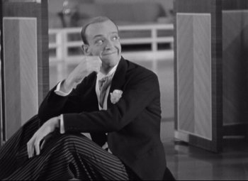Movie still from “Swing Time” (1936), directed by George Stevens – A man sitting on the ground wearing a suit and tie; Medium shot, Low angle